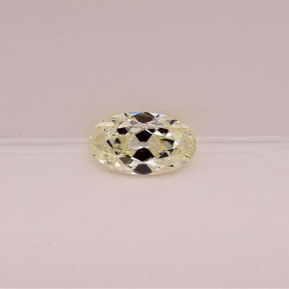 A single elongated oval-cut warm white diamond is set against a plain light pink background.