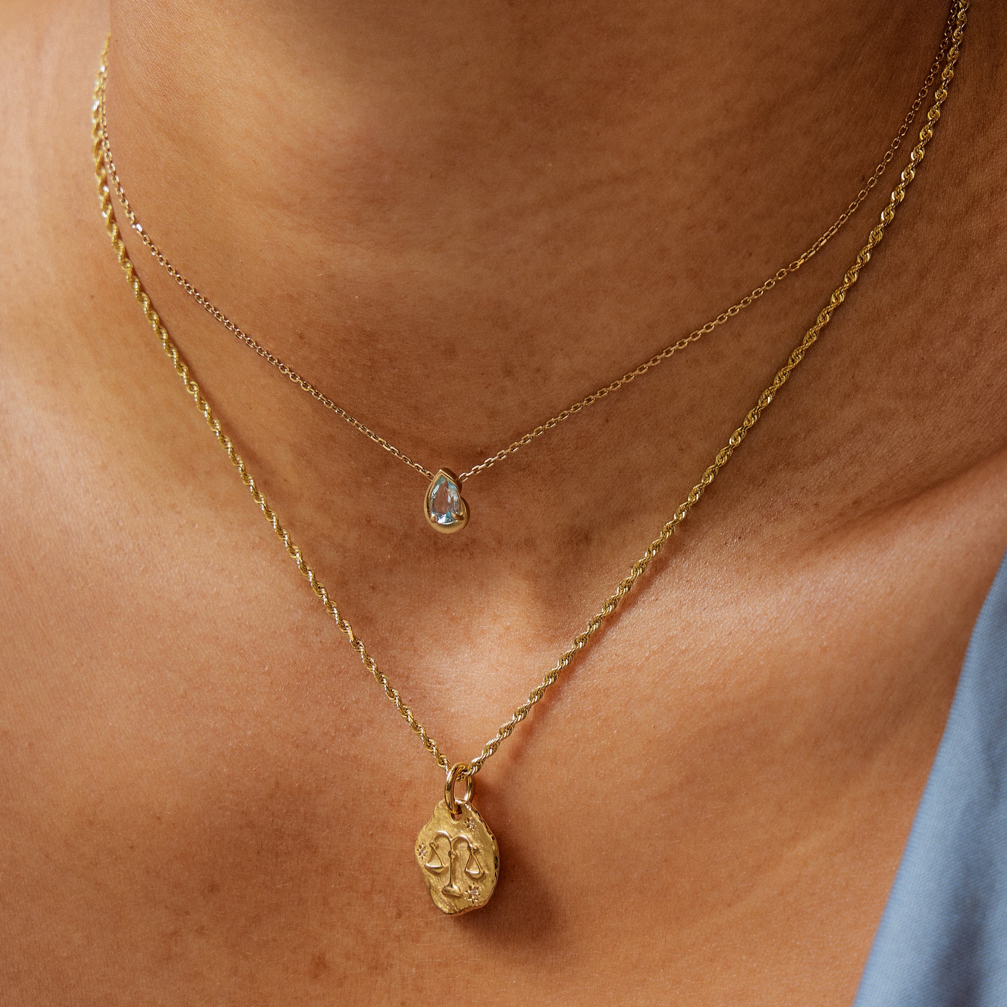 Close-up of a model wearing a BB Thelma Swiss Blue Topaz 14kt gold necklace + Zodiac Medallion with rope chain.
