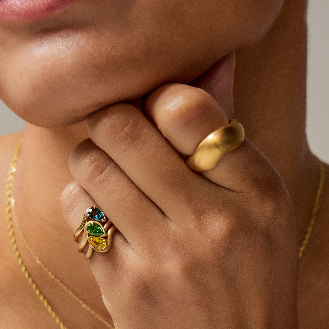 Hand model wearing BB Thelma pinky ring stack in teal sapphire, yellow sapphire, tsavorite garnet and sage band.