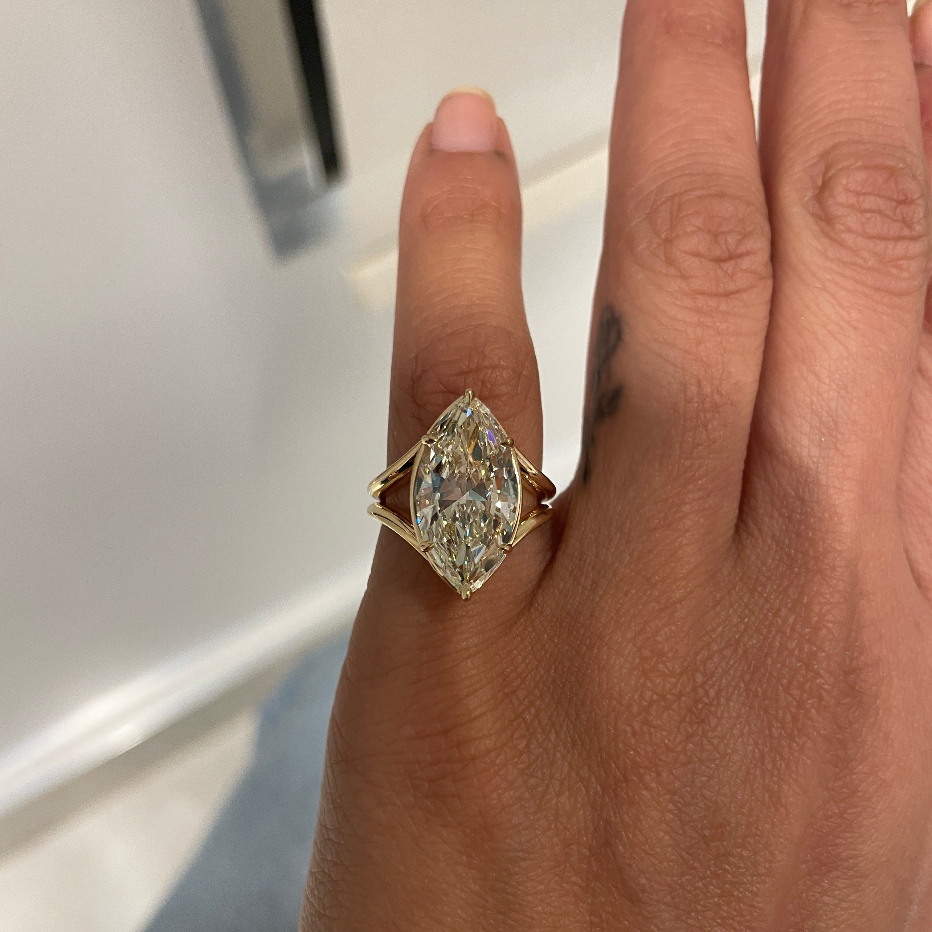 Hand wearing a gold ring with a diamond on a neutral background