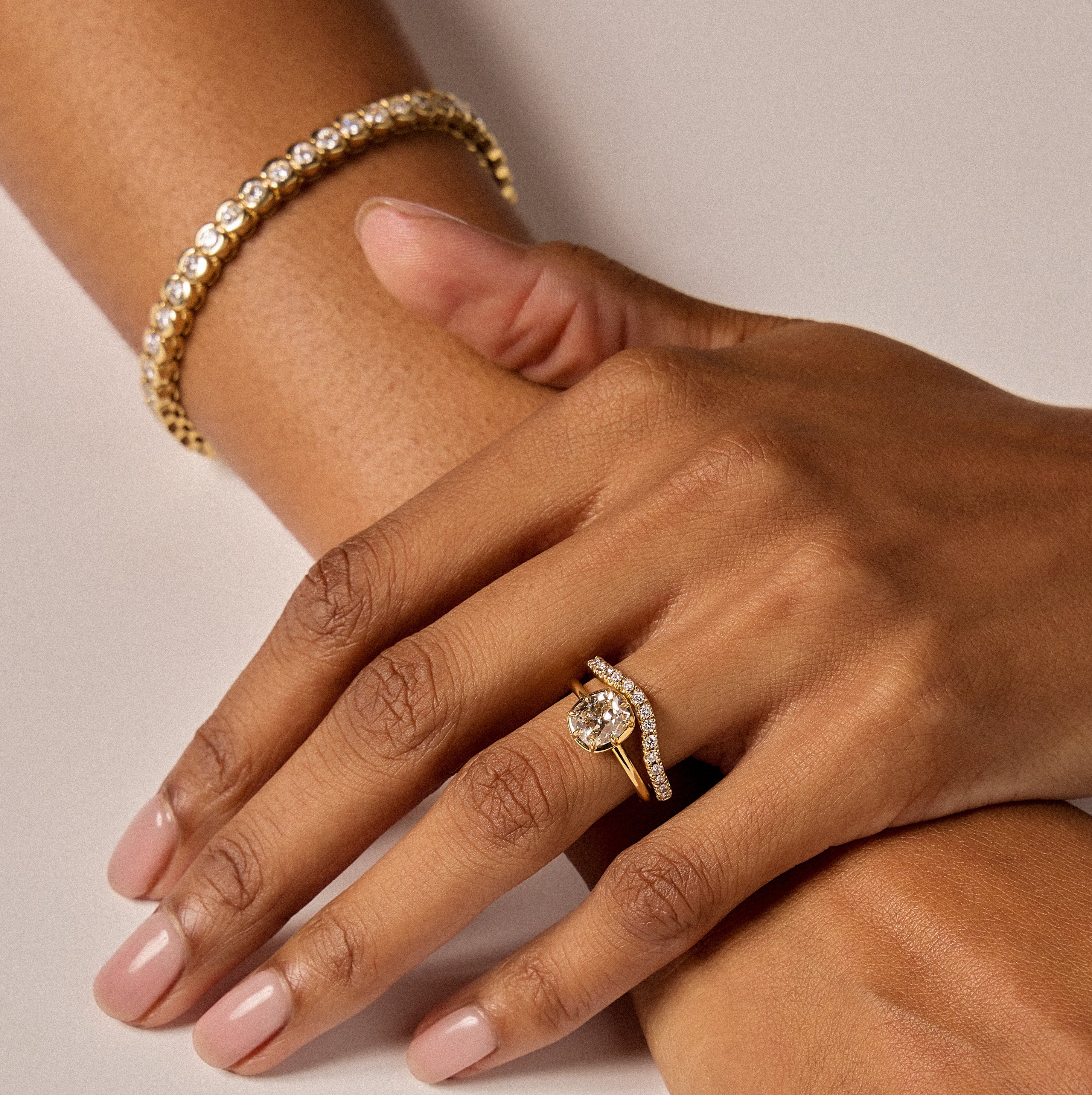 Close-up of hands wearing gold jewelry on a neutral background