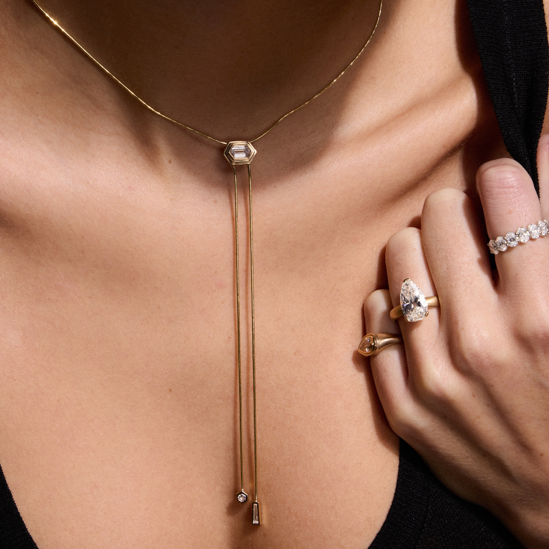 woman wearing gold and diamond lariat necklace with an assortment of diamond rings