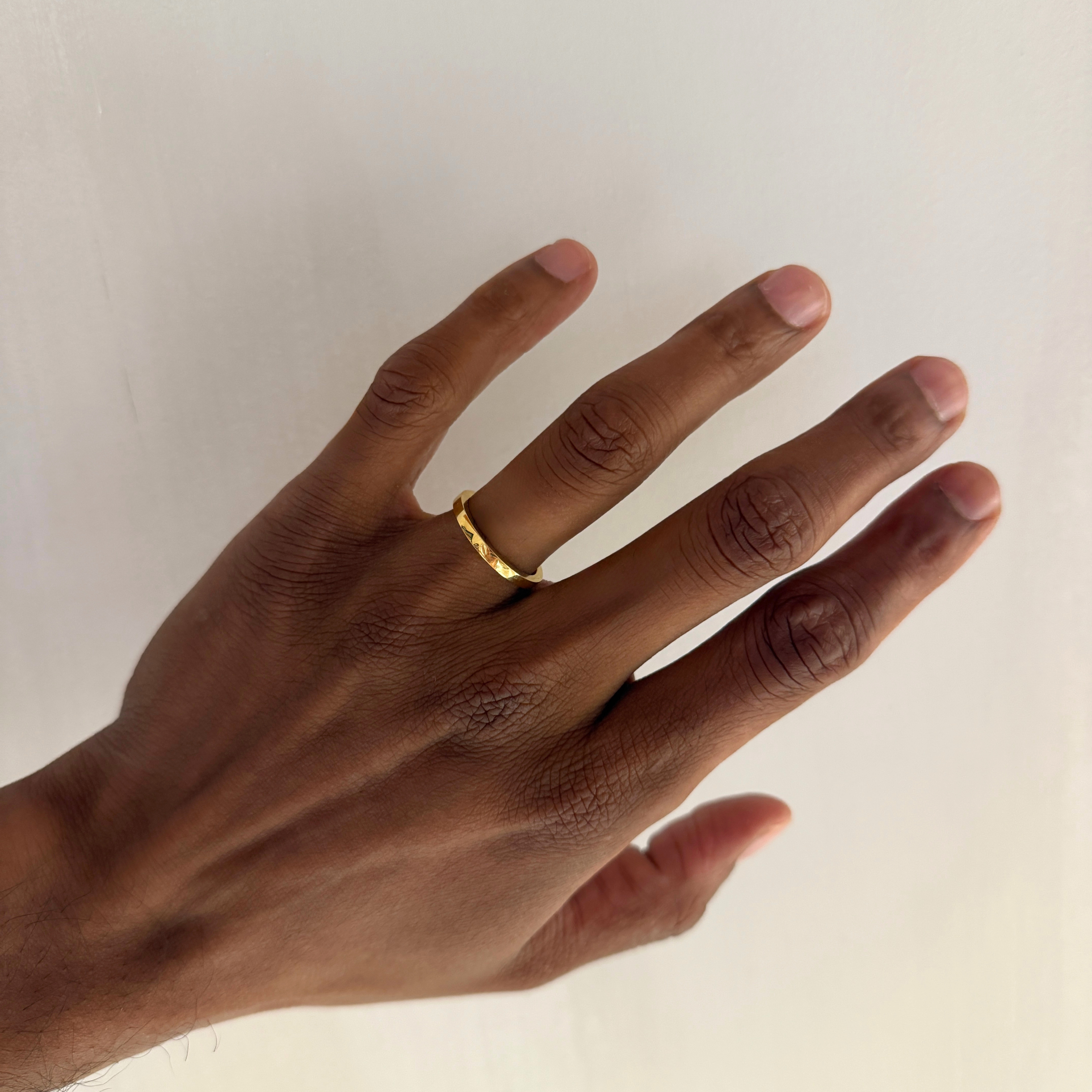 A gold high-shine wedding, ROCKY MEN's WEDDING BAND, ring worn on the ring finger of a person's hand, shown against a plain off-white background.