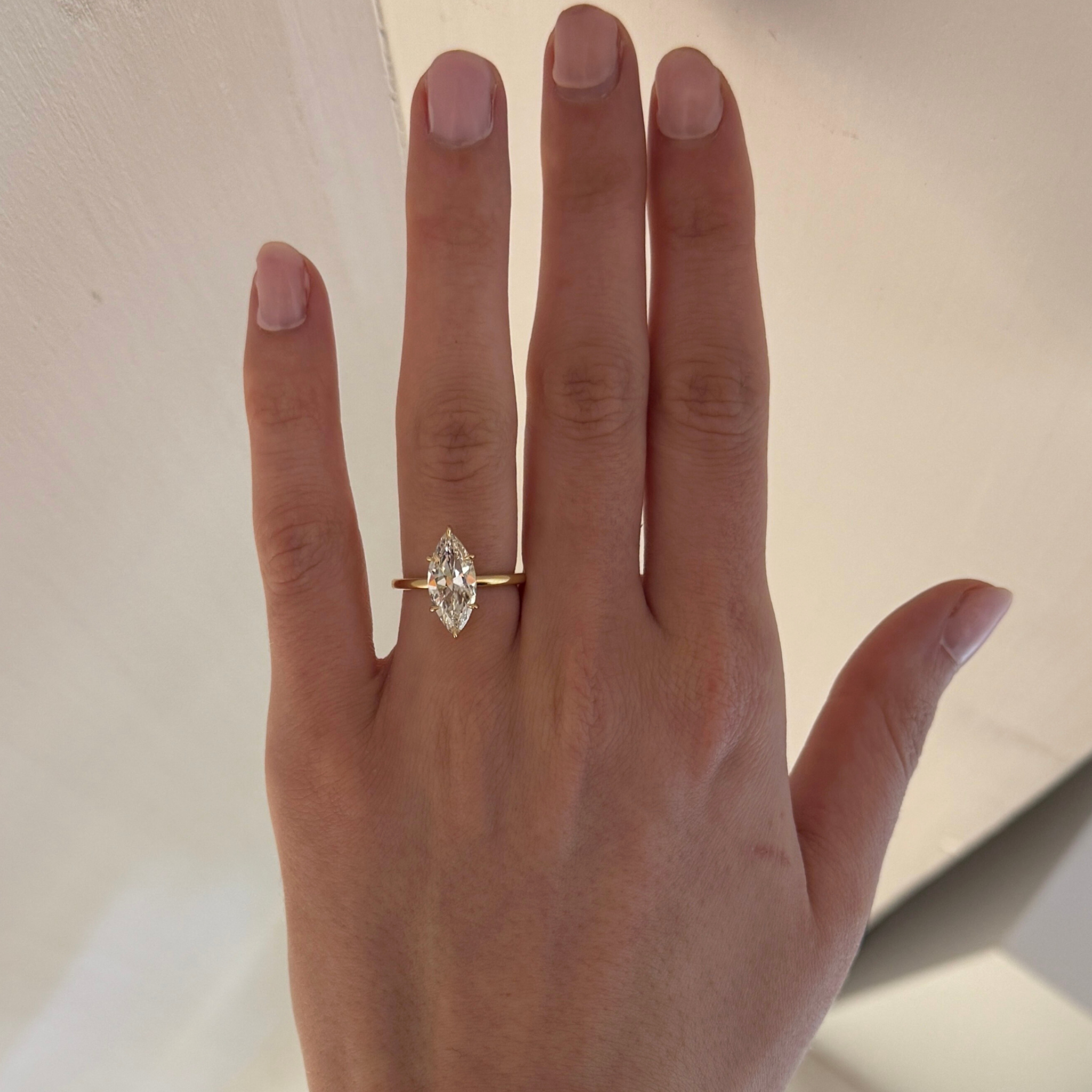 Hand wearing a gold ring with a diamond on a neutral background