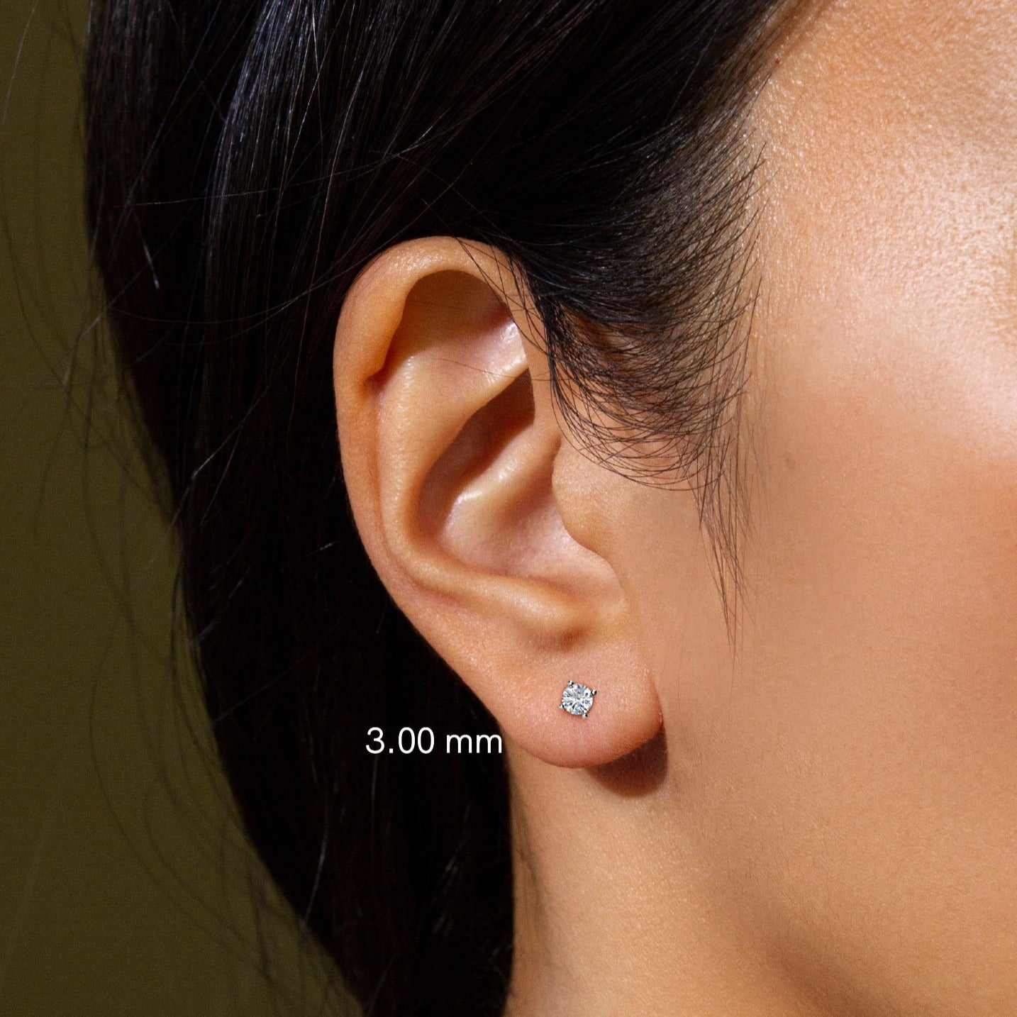 A pair of small, 3.0mm round, white gold diamond studs with push-back clasps on a model's ear.