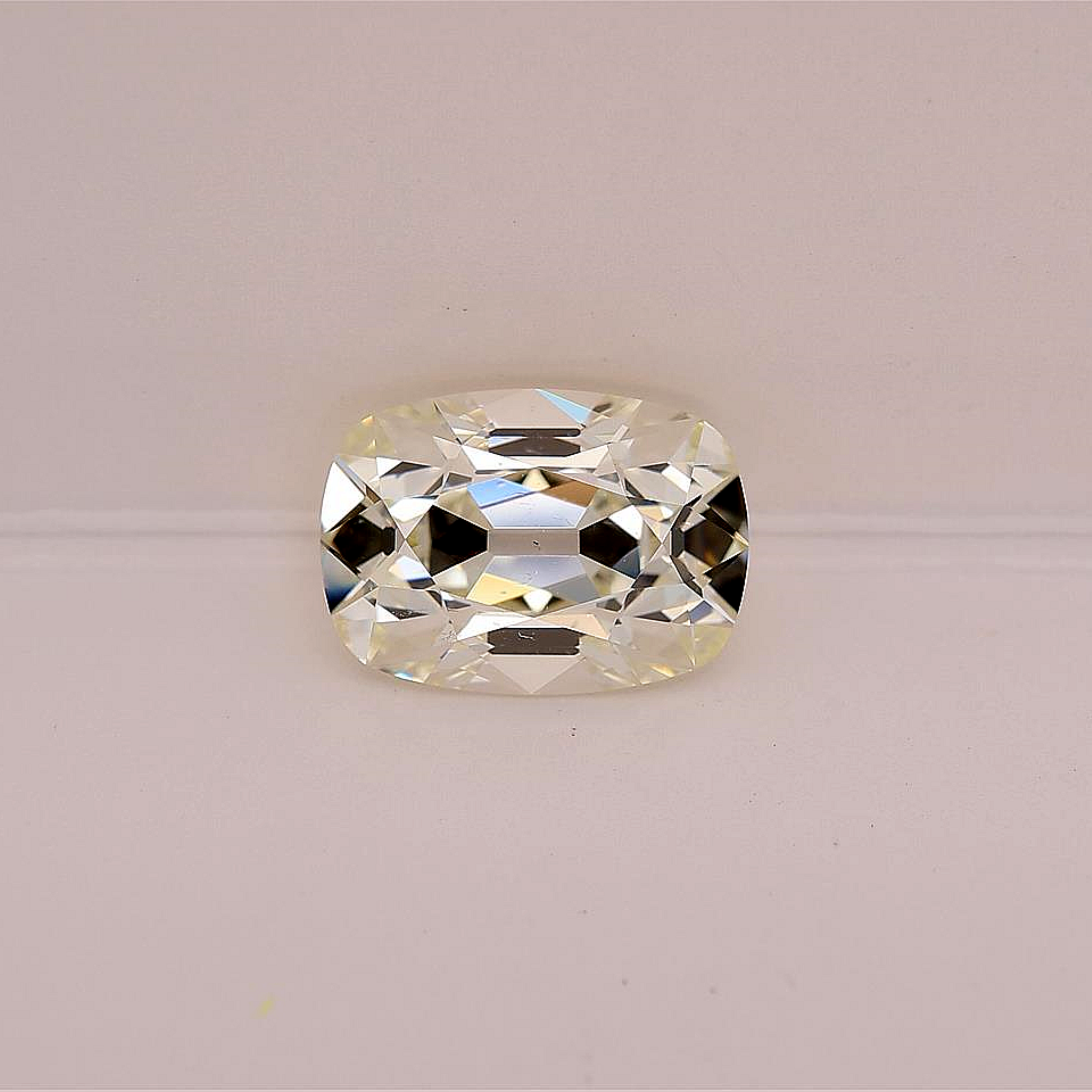 A old mine brilliant diamond with brilliant faceting, displayed on a clean, light pinkish-beige background.