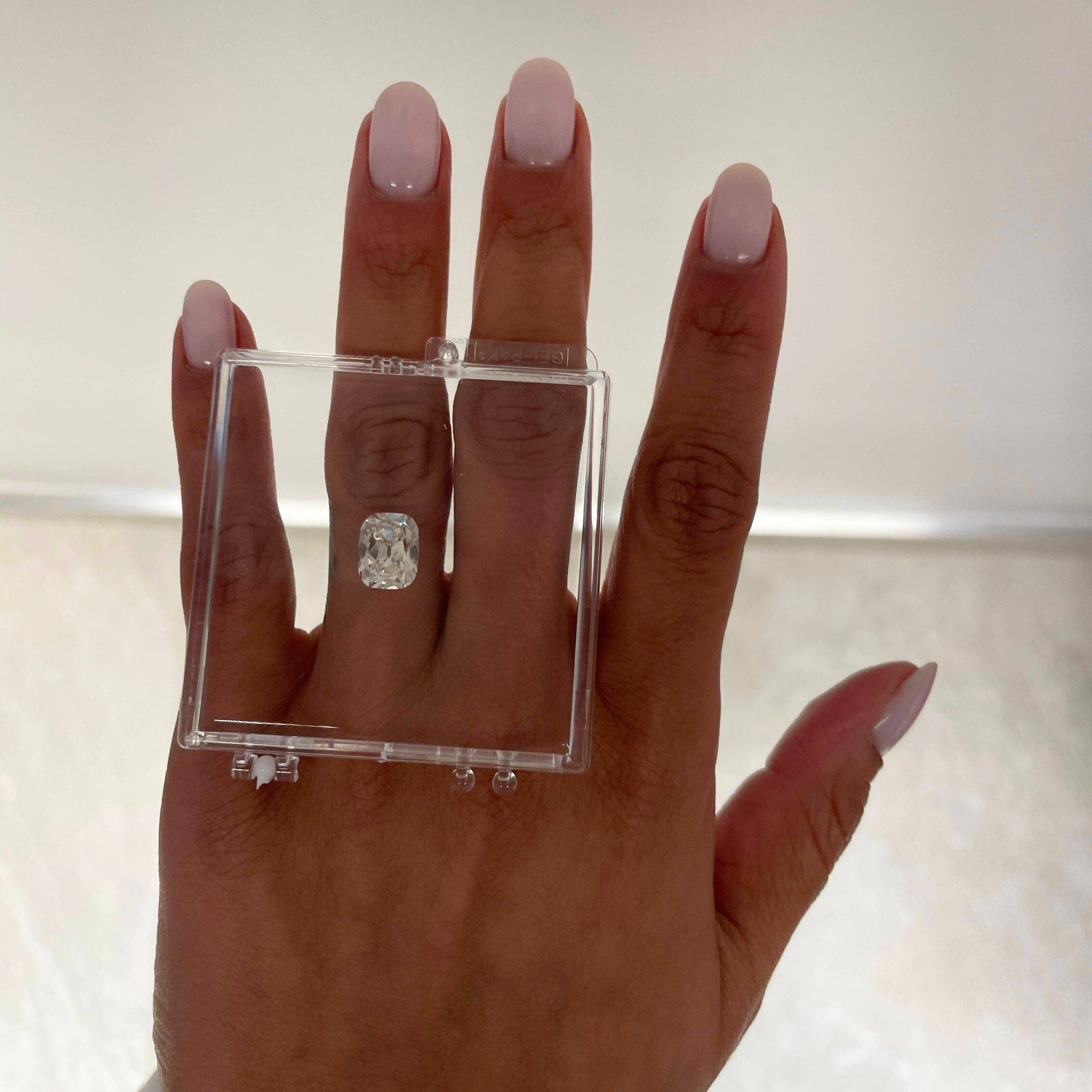 Hand wearing a clear ring box with a diamond on a neutral background