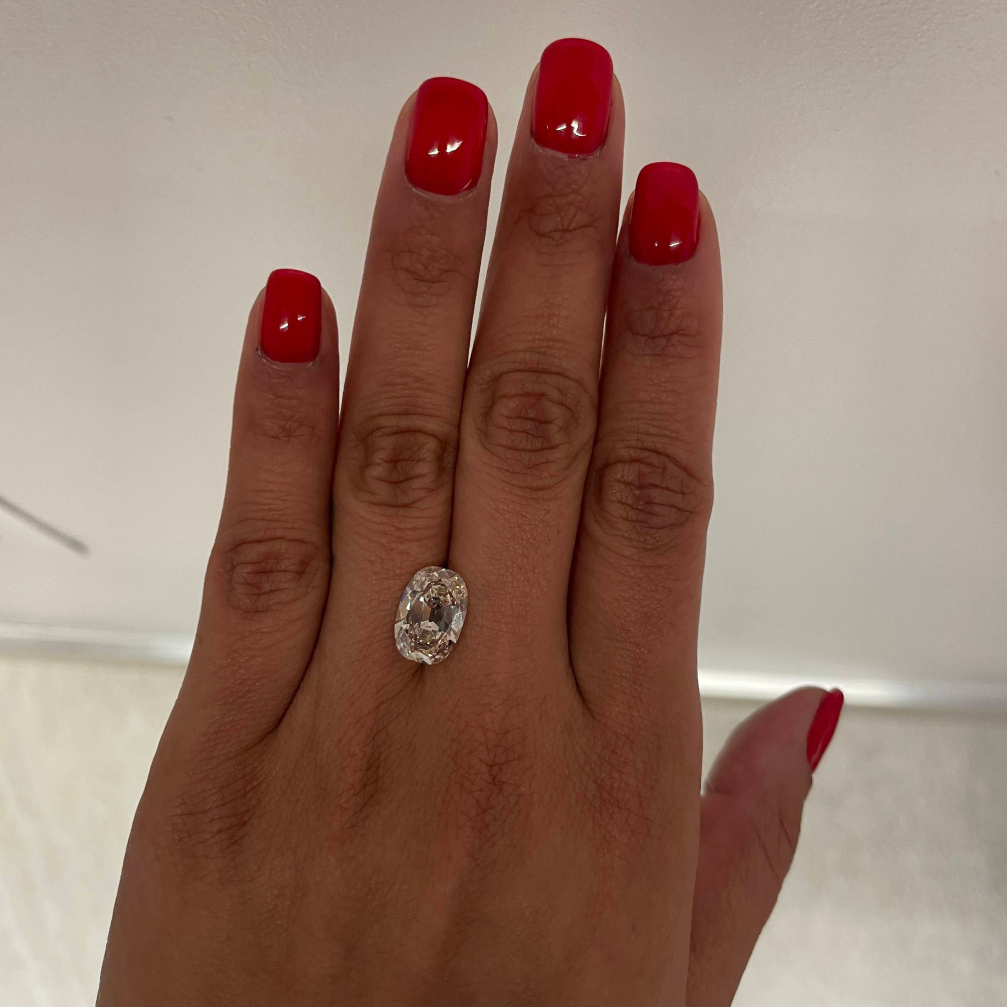 Hand with red nail polish wearing a diamond ring on a neutral background