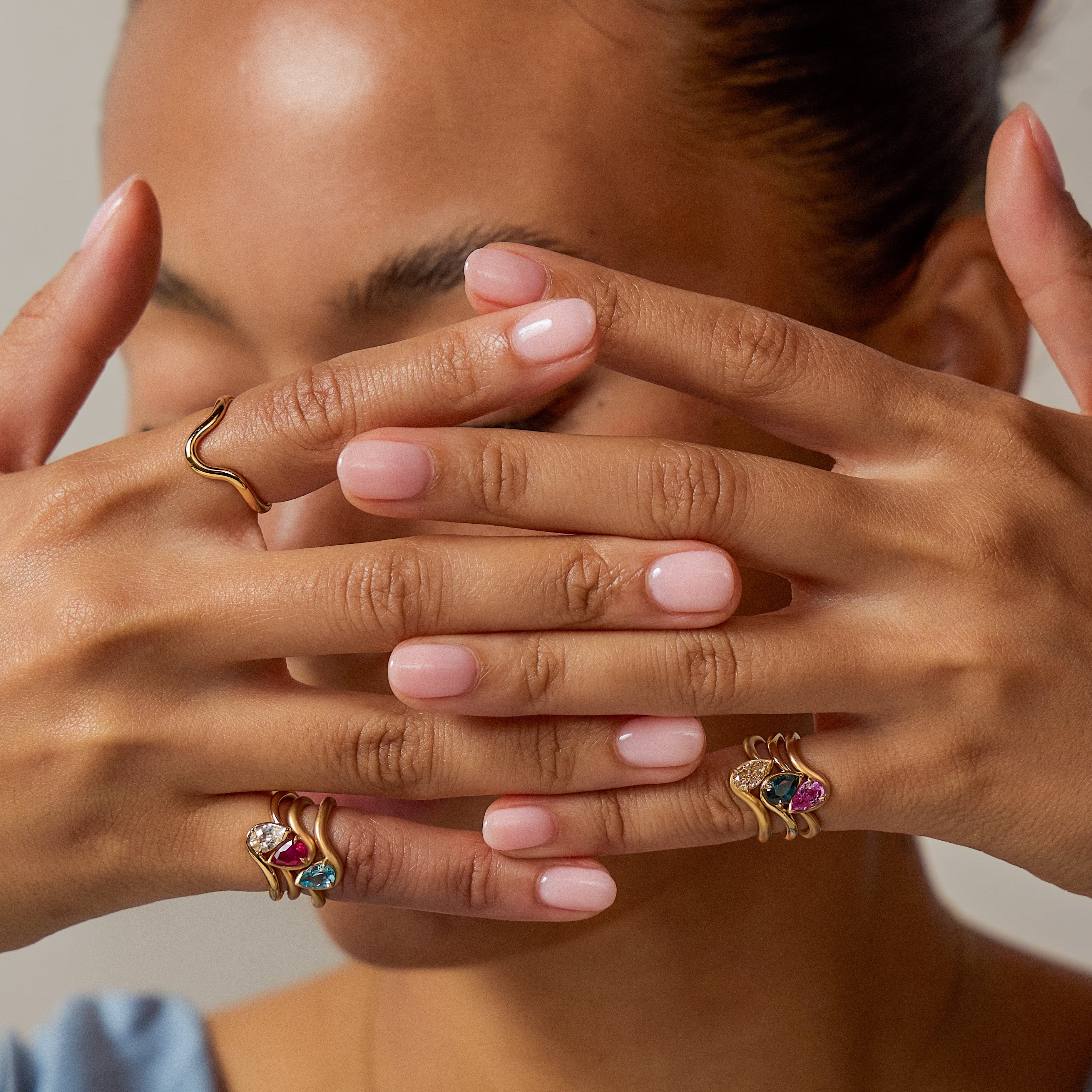 Hand model wearing BB thelma ring stack in blue swiss topaz, ruby, and white diamond on right pinky and brown diamond, blue sapphire, and pink sapphire on left pinky. 
