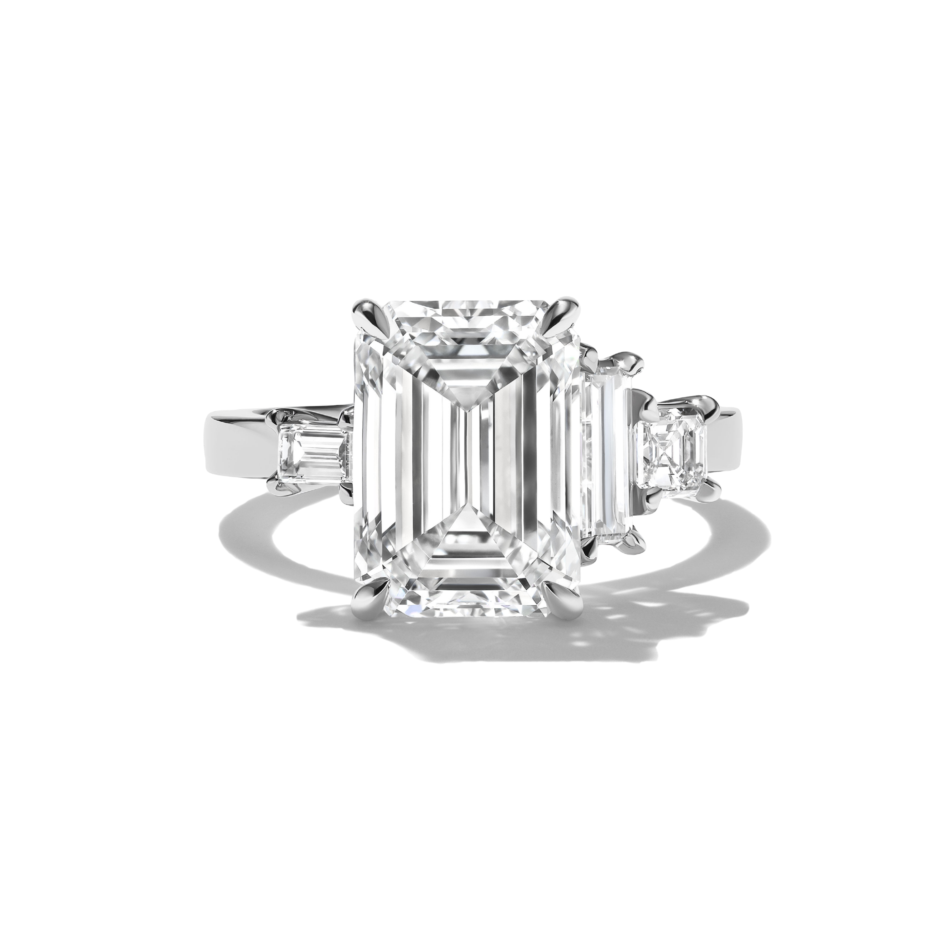 Diamond ring with emerald-cut center stone and baguette side stones on a white background
