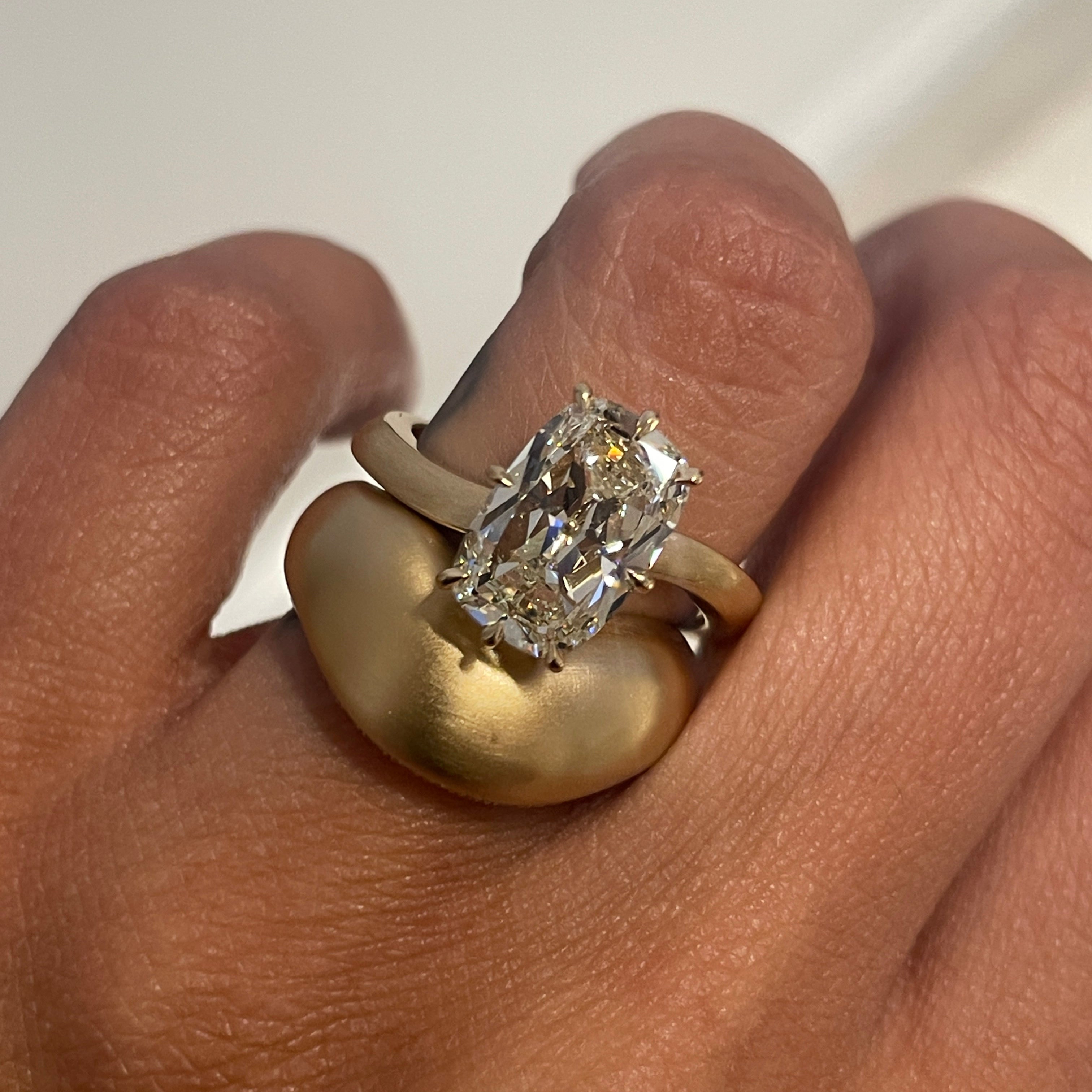 Gold ring with a diamond on a person's finger against a neutral background