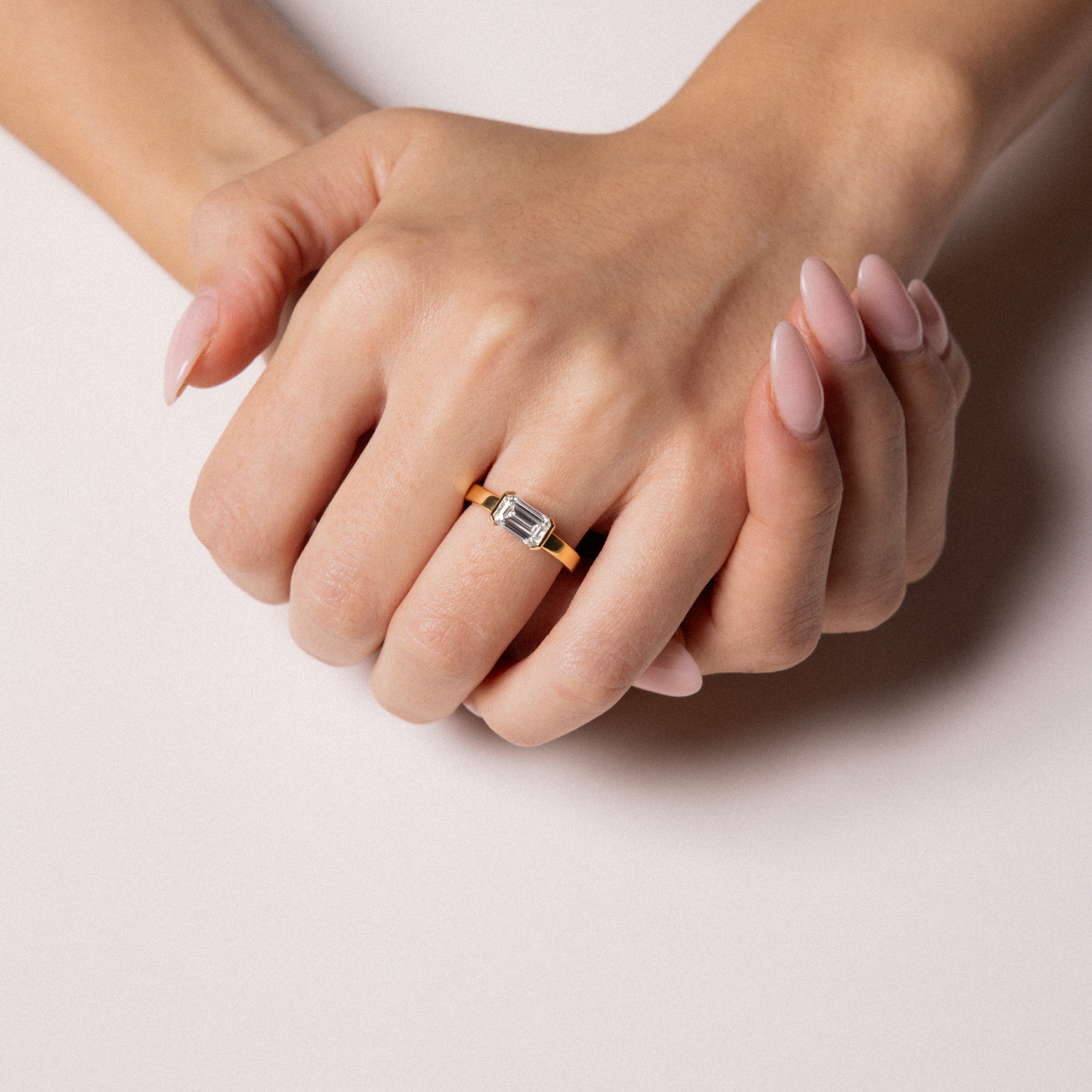 Close-up of a hand wearing a ring with a diamond on a light background