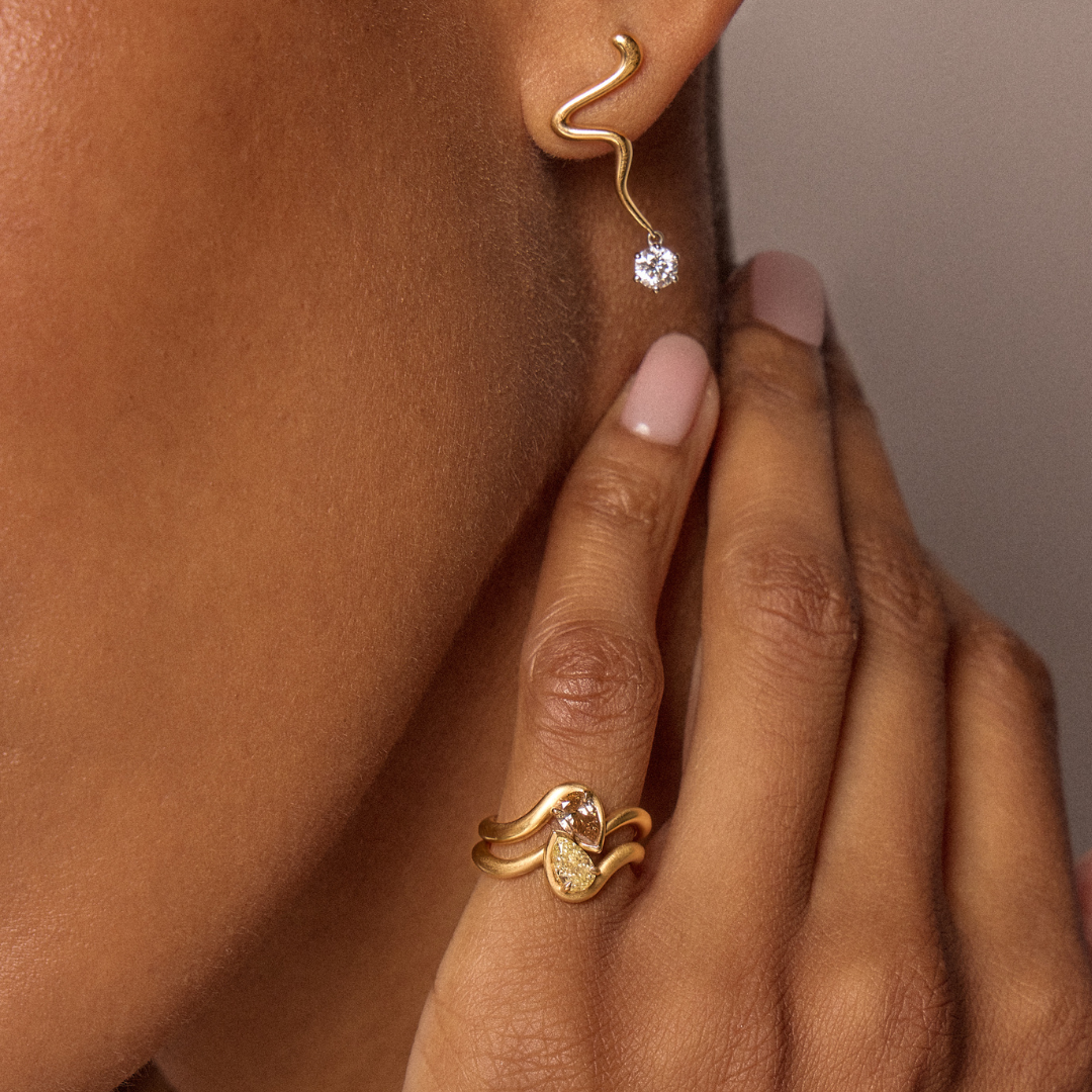 Model wearing BB Thelma pinky rings in brown diamond + yellow diamond and Maia squiggle drop earrings. All 14k yellow gold