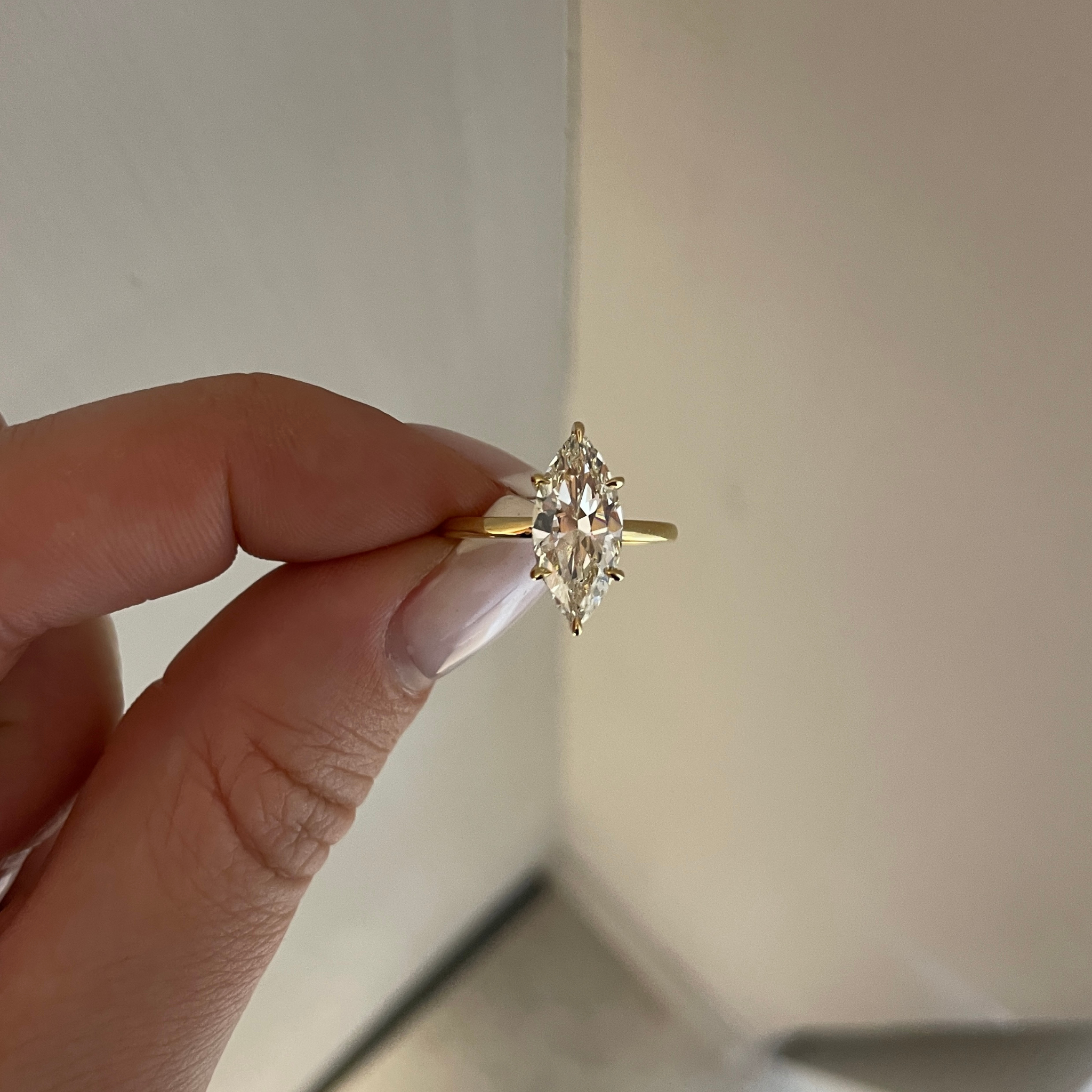 Gold ring with a diamond held by a hand against a neutral background
