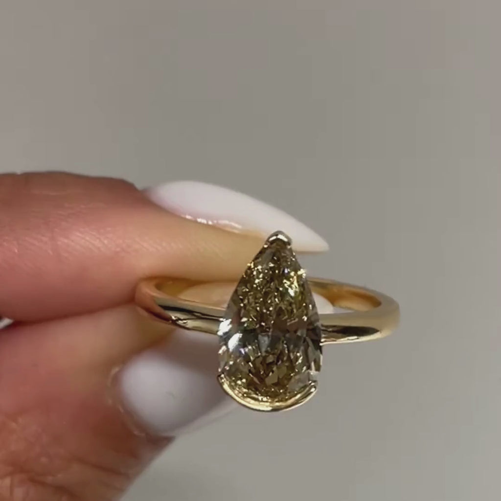 Bespoke Brown Pear cut diamond, in Jupiter setting, 18kt Yellow Gold in high Shine finish.  Close Up between fingers.