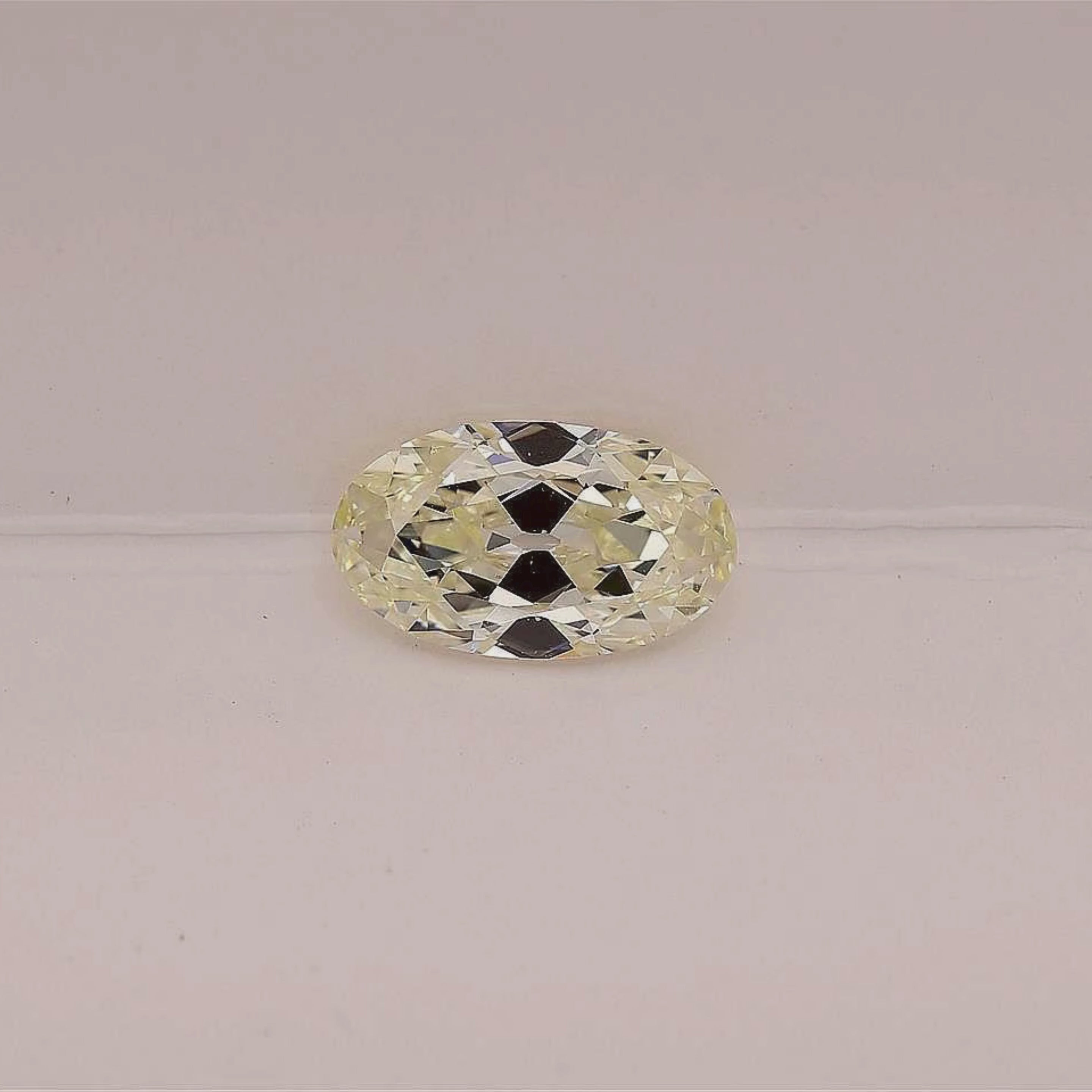 A single elongated oval-cut warm white diamond is set against a plain light pink background.