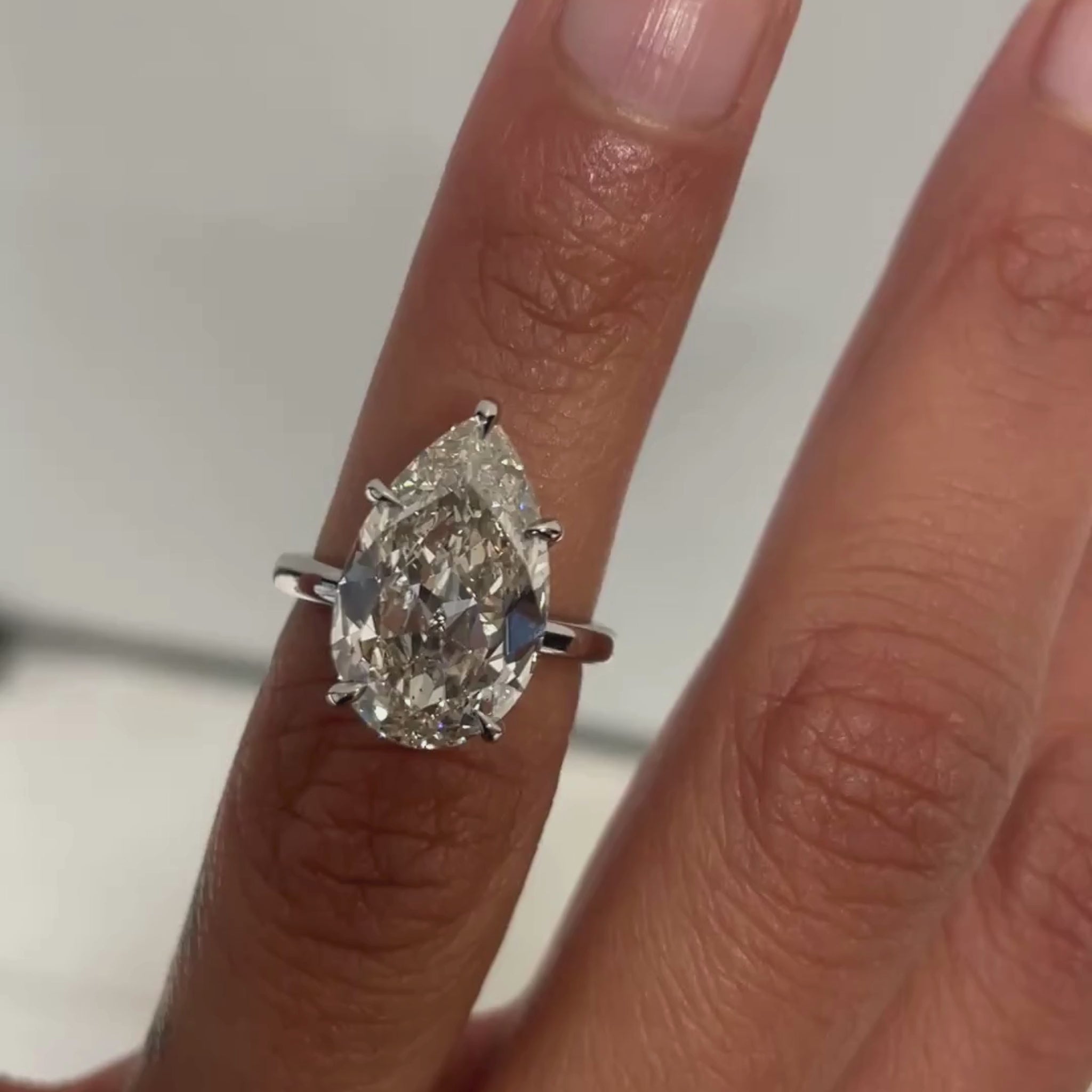 Bespoke Acacia Engagement Ring with Light Brown Pear Cut Diamond on a high shine platinum band, on finger, close up. 