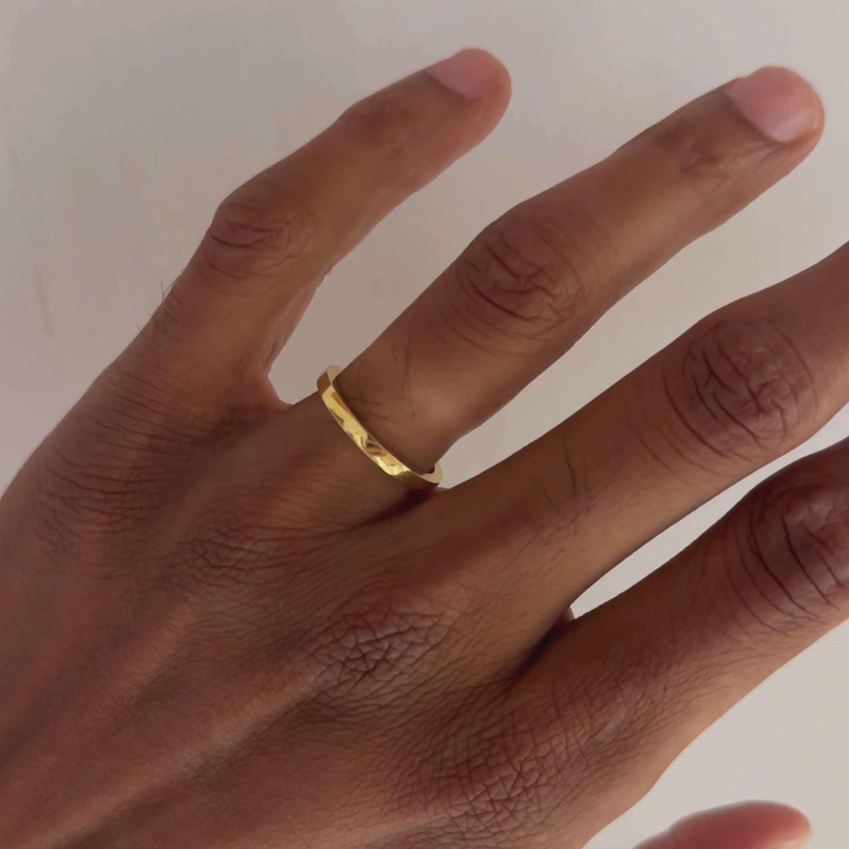 A gold high-shine wedding, ROCKY MEN's WEDDING BAND, ring worn on the ring finger of a person's hand, shown against a plain off-white background.